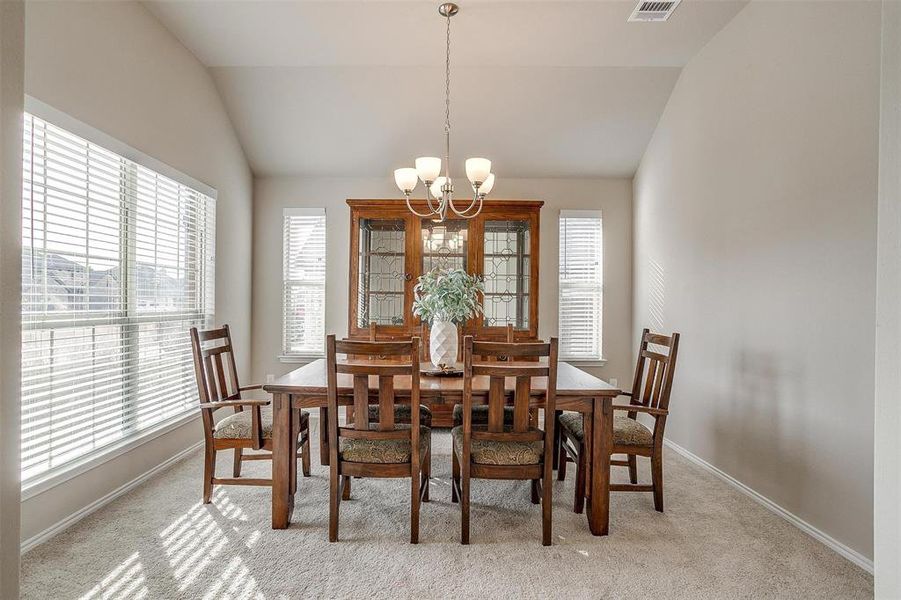 Carpeted dining space with plenty of natural light, vaulted ceiling, and an inviting chandelier