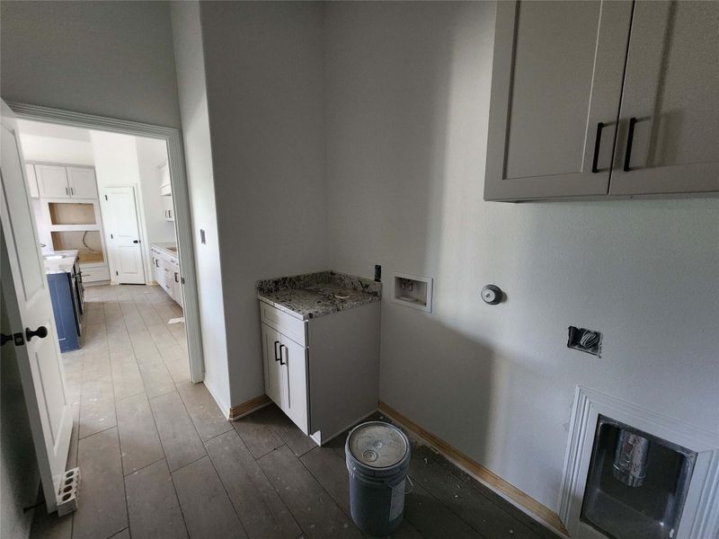 Laundry area featuring wood-finish flooring, white cabinetry, granite-style countertop, and upper wall cabinets with black hardware