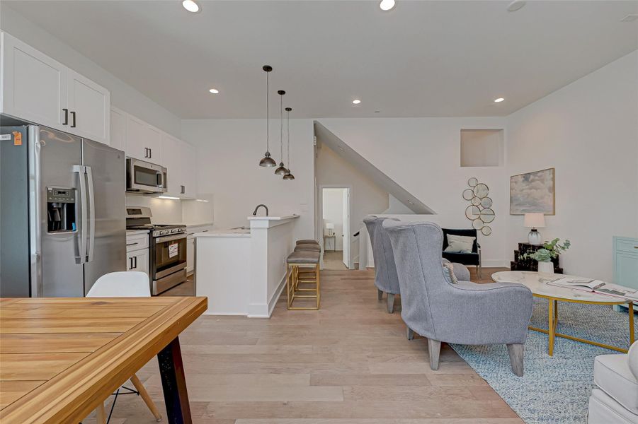 Bright, functional, and beautifully integrated, this open-concept space seamlessly connects the chef’s kitchen, breakfast bar, and cozy living area. Pendant lighting, quartz countertops, and warm wood floors enhance the modern yet inviting atmosphere.