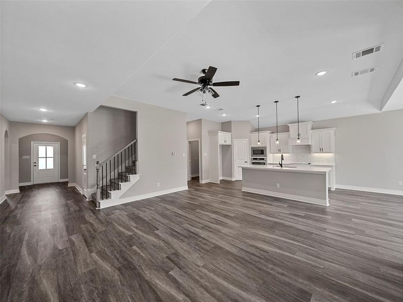 Unfurnished living room featuring dark wood-style floors, stairs, a ceiling fan, arched walkways, and recessed lighting Unfurnished living room featuring dark wood-style floors, stairs, a ceiling fan, arched walkways, and recessed lighting