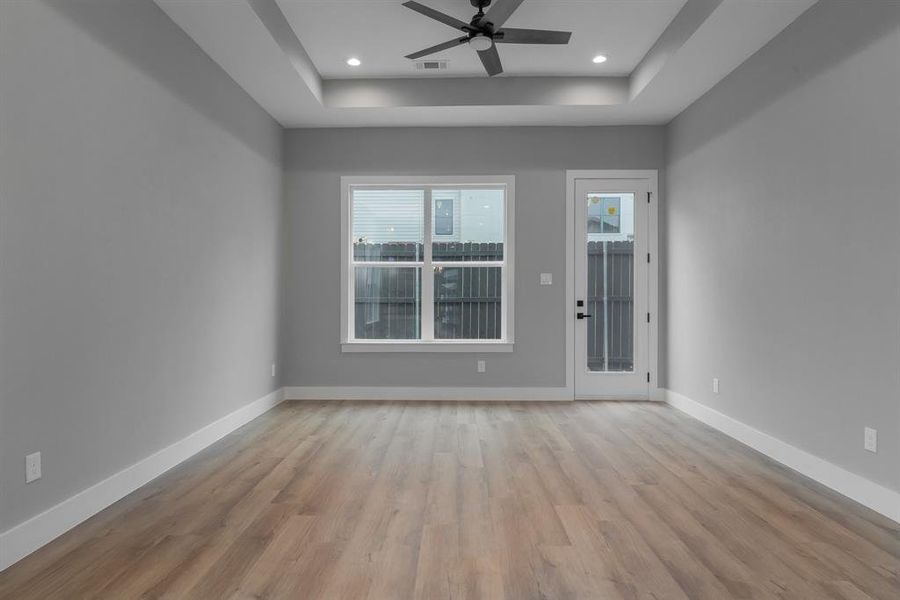 Unfurnished room featuring light wood-type flooring, visible vents, a ceiling fan, a tray ceiling, and baseboards