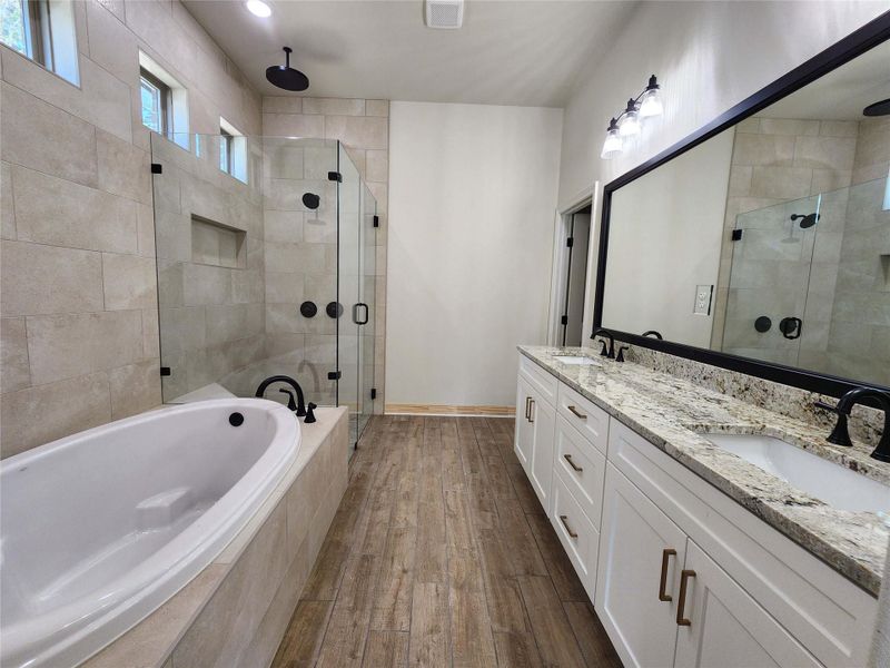 Full bathroom with double vanity, a garden tub, a shower stall, and dark wood-style floors