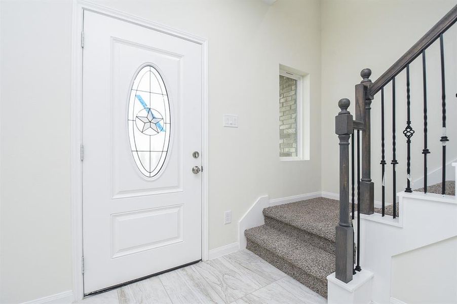 A home interior foyer with a white door featuring stained glass, carpeted stairs, and a black metal stair railing.