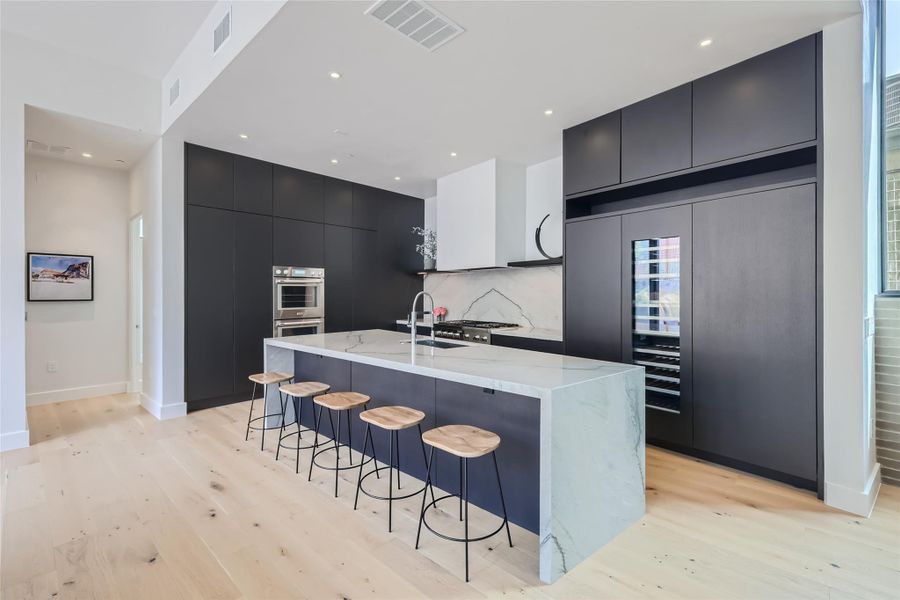 A contemporary kitchen features sleek dark cabinetry, integrated appliances, and a grand marble island with seating. A contemporary kitchen features sleek dark cabinetry, integrated appliances, and a grand marble island with seating.