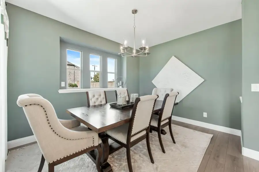 Dining room with dark wood table, upholstered chairs, chandelier, and sage green walls