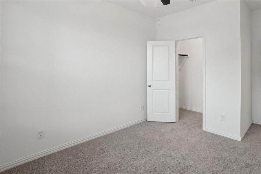 Unfurnished bedroom featuring light carpet, a closet, a spacious closet, and ceiling fan