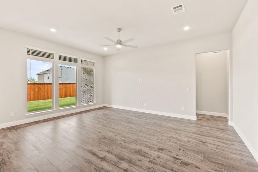 Empty living room with wood-look floors, ceiling fan, and large windows overlooking a fenced backyard Empty living room with wood-look floors, ceiling fan, and large windows overlooking a fenced backyard