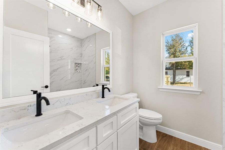 Full bath with dark wood finished floors, double vanity, and plenty of natural light