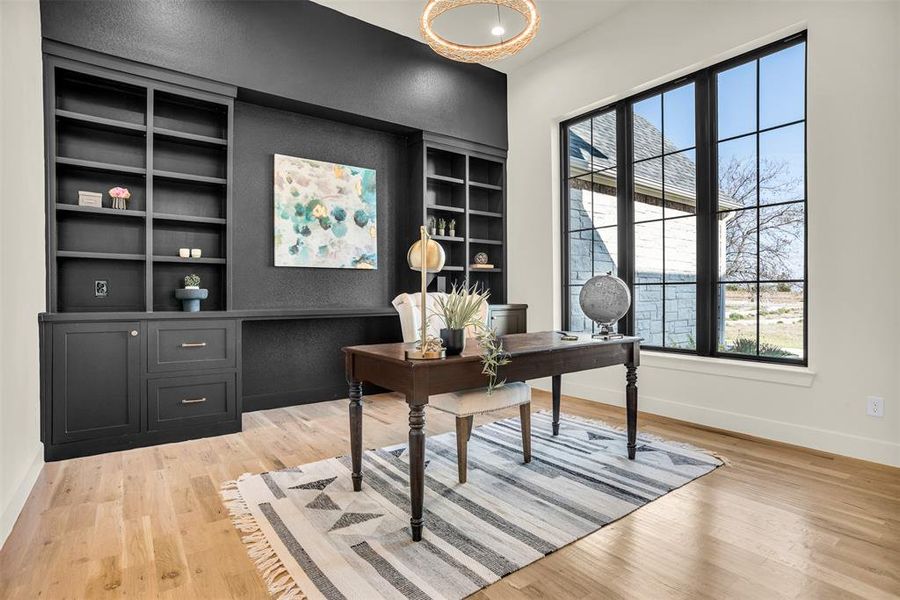 Office space with built in features, light wood finished floors, and a textured wall