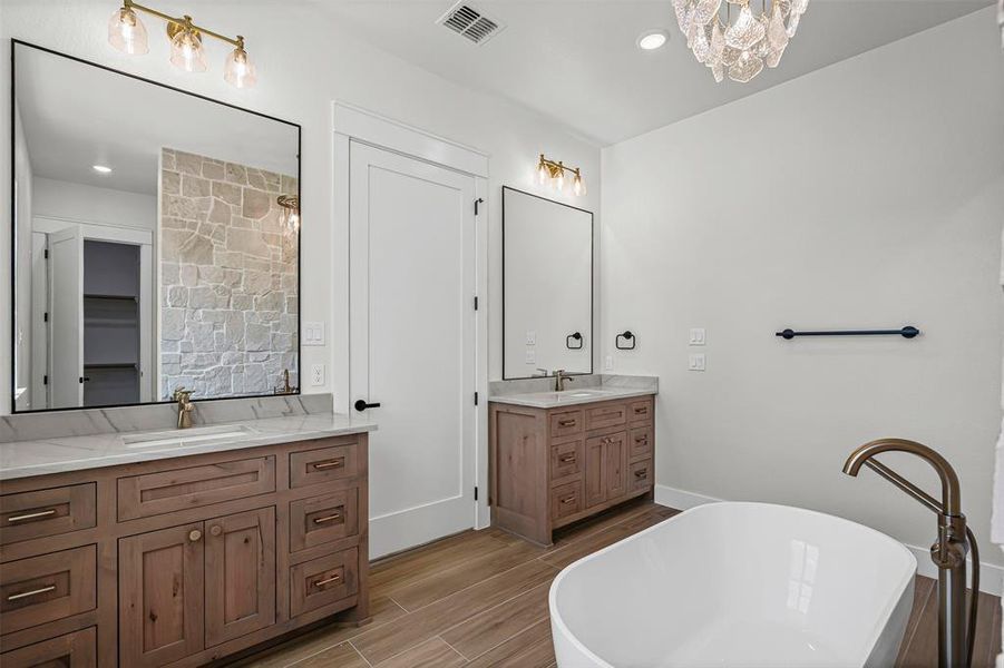 Full bathroom with a freestanding tub, two vanities, wood tiled floors, recessed lighting, and a chandelier Full bathroom with a freestanding tub, two vanities, wood tiled floors, recessed lighting, and a chandelier