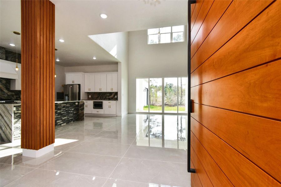 Step through the custom wood-pivot door into an airy, open-concept floor plan. Polished porcelain tile floors and high-volume ceilings create a sophisticated, light-filled atmosphere.
