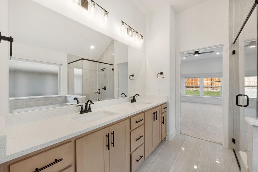Master bathroom with double vanity, quartz countertops, glass shower, and tile floors