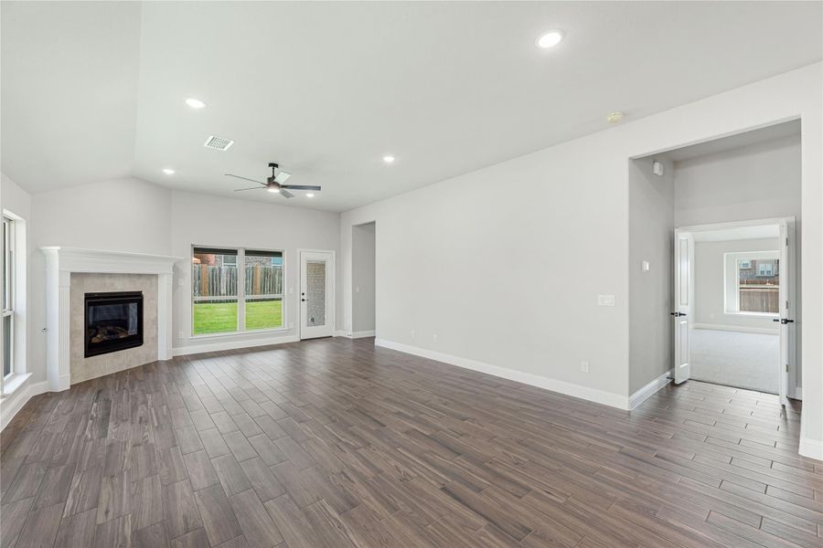 Open living room with vaulted ceiling, tile fireplace, ceiling fan, and dark wood-look floors Open living room with vaulted ceiling, tile fireplace, ceiling fan, and dark wood-look floors