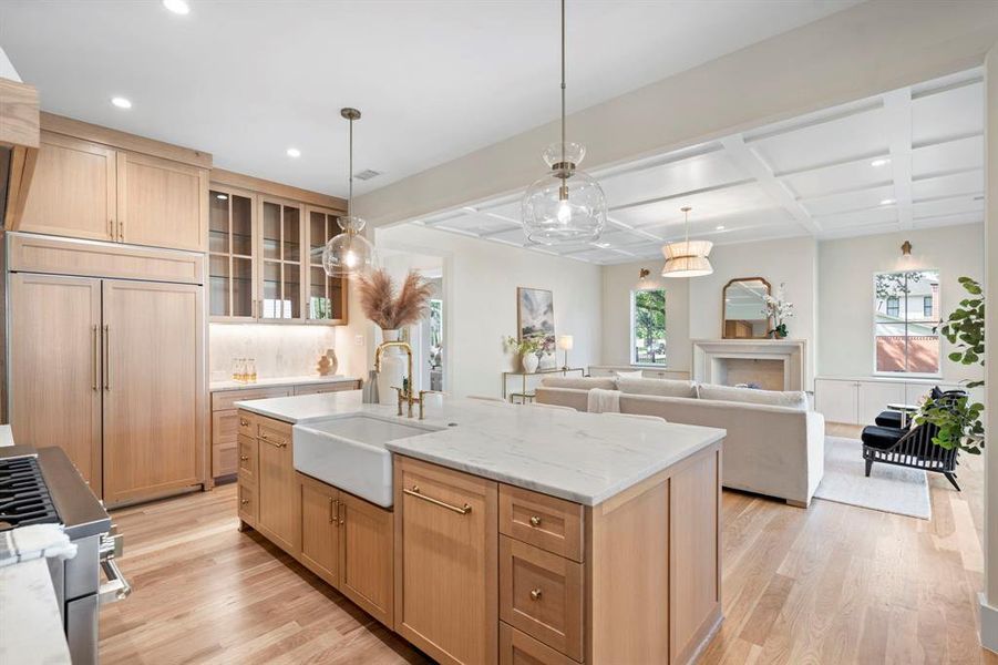 Kitchen featuring hanging light fixtures, sink, coffered ceiling, a center island with sink, and light hardwood / wood-style floors