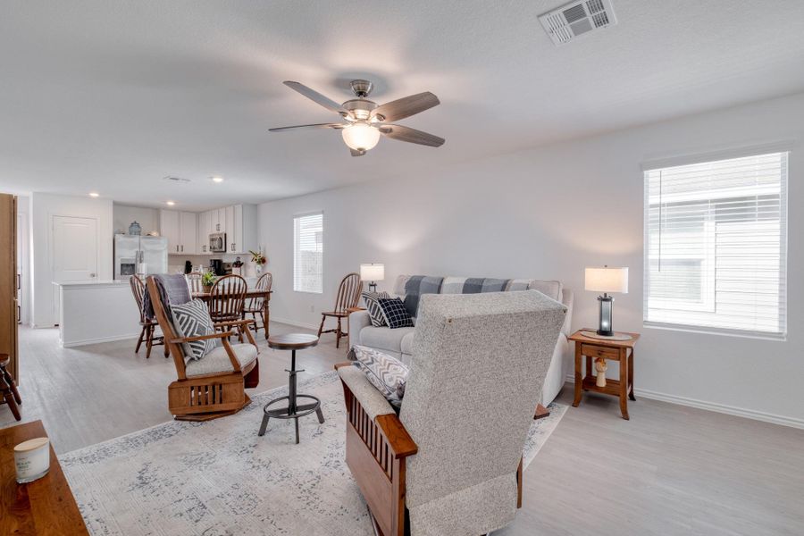 The property offers an open concept living area featuring light-toned flooring, a ceiling fan with integrated lighting, and windows with blinds