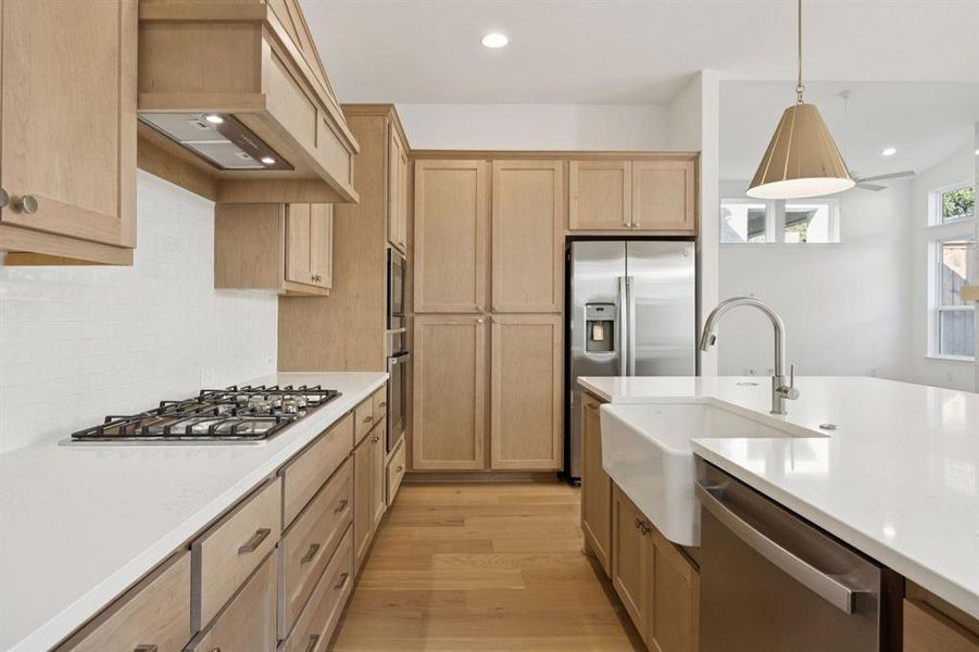 Kitchen with light wood-style flooring, stainless steel appliances, hanging light fixtures, and light stone counters Kitchen with light wood-style flooring, stainless steel appliances, hanging light fixtures, and light stone counters