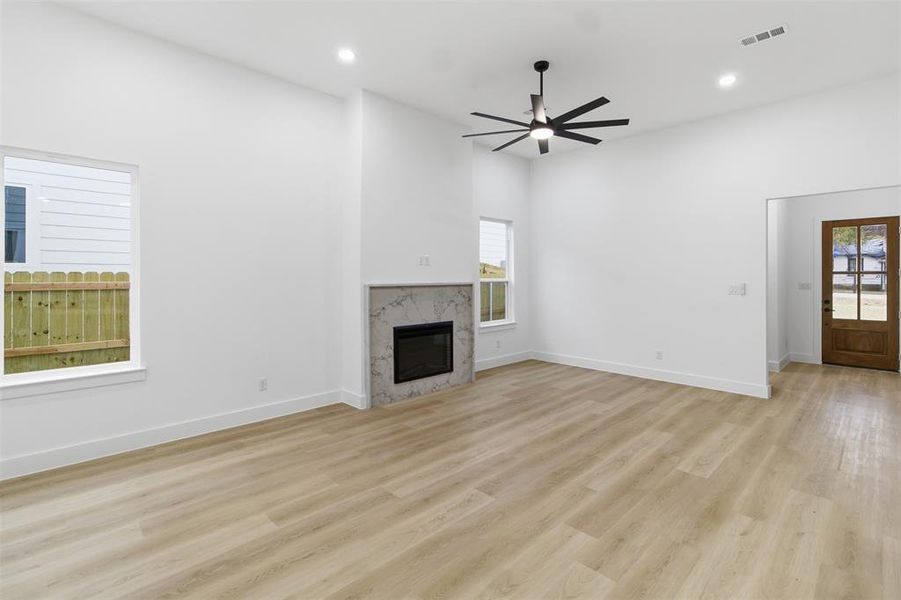 Unfurnished living room with a high end fireplace, light wood finished floors, recessed lighting, healthy amount of natural light, and ceiling fan