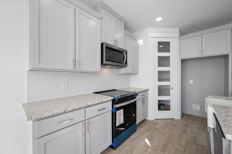 Kitchen featuring black / electric stove, light stone countertops, and light hardwood / wood-style flooring