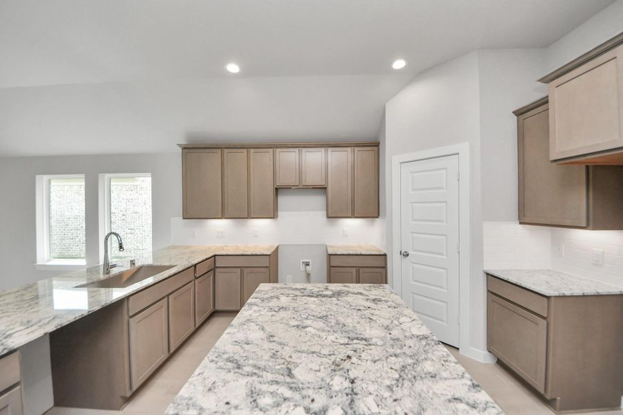 The kitchen is a culinary haven, featuring granite countertops, a tile backsplash, stainless steel appliances, 42” upper cabinets, and undercabinet lighting. Sample photo of completed home with similar floor plan. Actual colors and selections may vary.