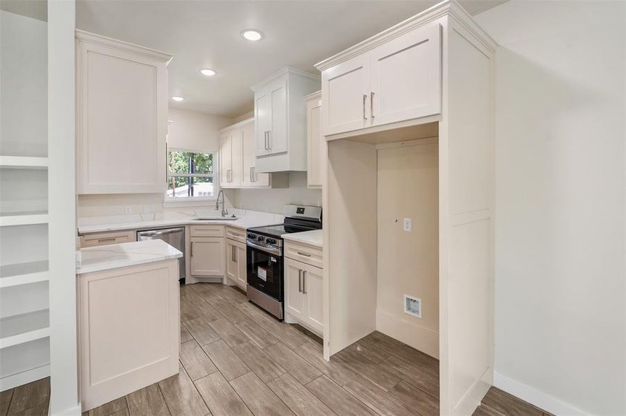 Bright kitchen featuring white shaker cabinetry, stainless steel appliances, wood-finish flooring, recessed lighting, and a built-in pantry cabinet Bright kitchen featuring white shaker cabinetry, stainless steel appliances, wood-finish flooring, recessed lighting, and a built-in pantry cabinet