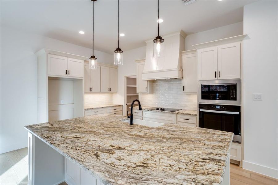 Kitchen featuring stainless steel appliances, light stone countertops, pendant lighting, a center island with sink, and white cabinets