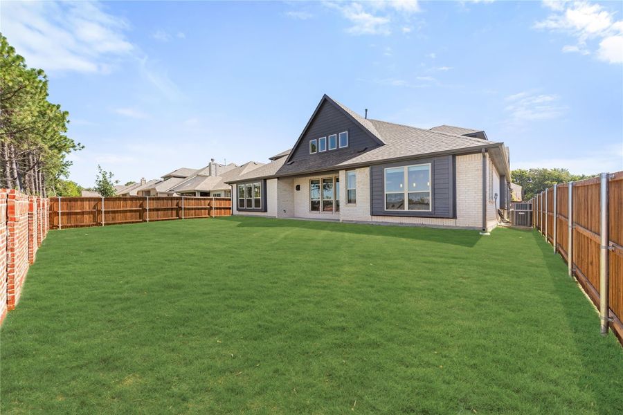 Backyard of a two-story brick home with large green lawn and wood privacy fence