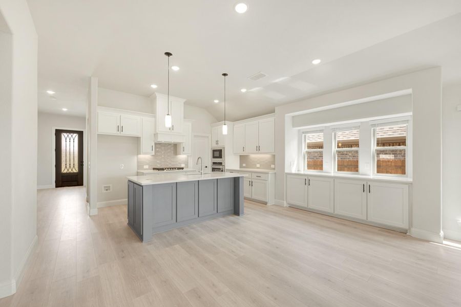 Open kitchen with white cabinets, gray island, pendant lights, and light hardwood floors