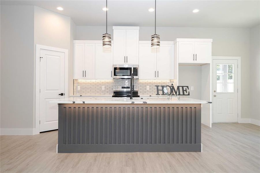 Kitchen featuring a kitchen island with sink, white cabinetry, pendant lighting, light stone counters, and light wood finished floors Kitchen featuring a kitchen island with sink, white cabinetry, pendant lighting, light stone counters, and light wood finished floors