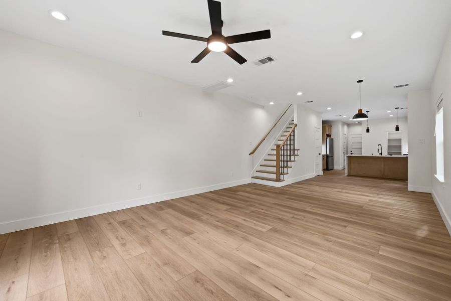Spacious open-concept living area with sleek wood flooring, modern ceiling fan, and recessed lighting, seamlessly flowing into a stylish kitchen with pendant lights and a central island.