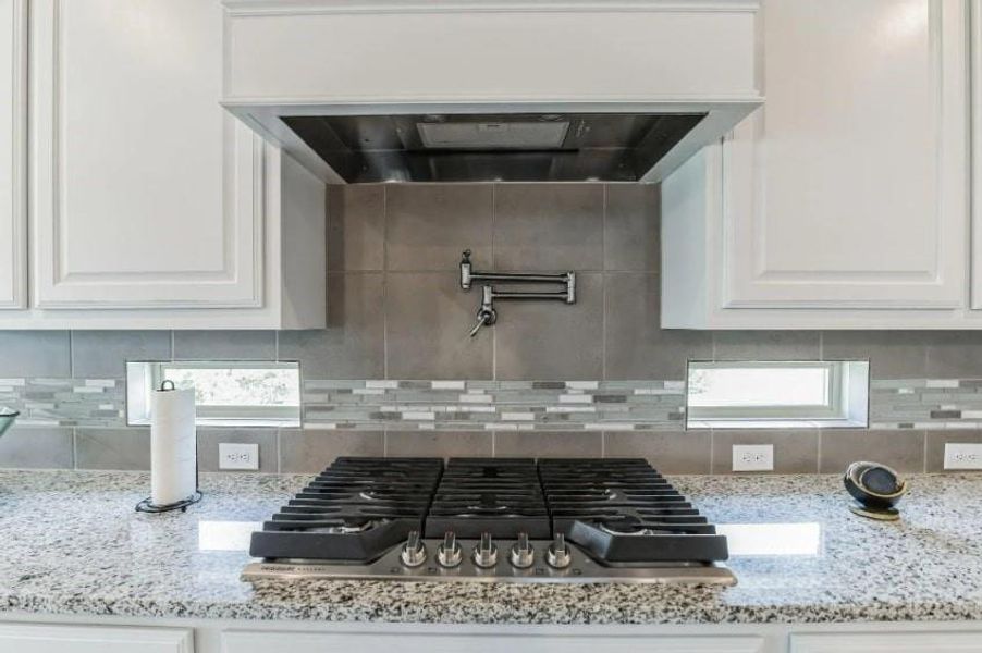 Kitchen with stainless steel gas cooktop, white cabinetry, backsplash, and light stone counters