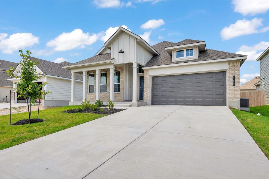 View of front facade featuring brick siding, roof with shingles, covered porch, driveway, and a front lawn