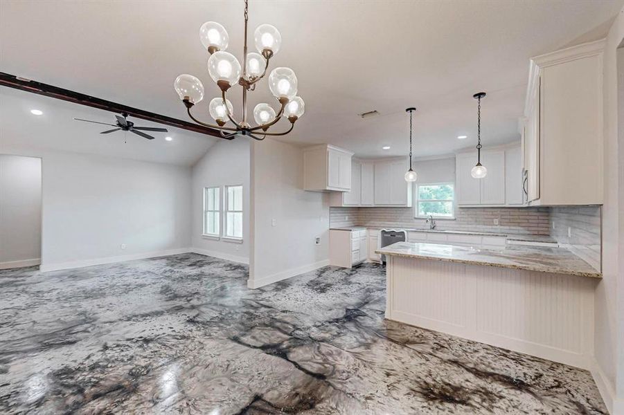 Kitchen featuring decorative backsplash, light stone countertops, ceiling fan with notable chandelier, white cabinets, and vaulted ceiling with beams