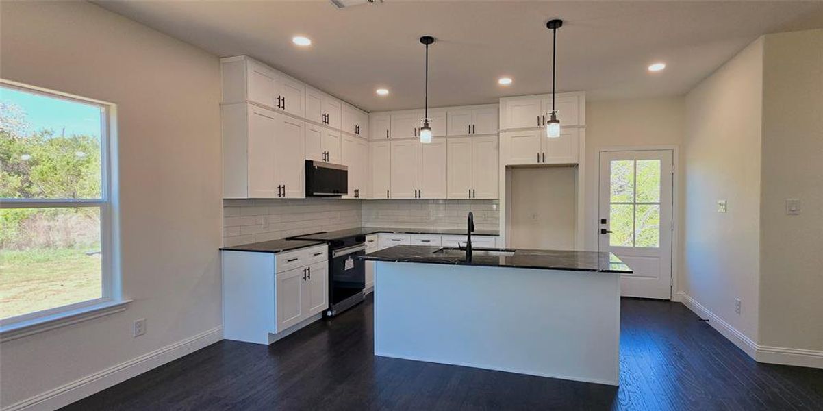 Kitchen with white cabinets, stainless steel appliances, dark wood finished floors, a kitchen island with sink, and hanging light fixtures Kitchen with white cabinets, stainless steel appliances, dark wood finished floors, a kitchen island with sink, and hanging light fixtures