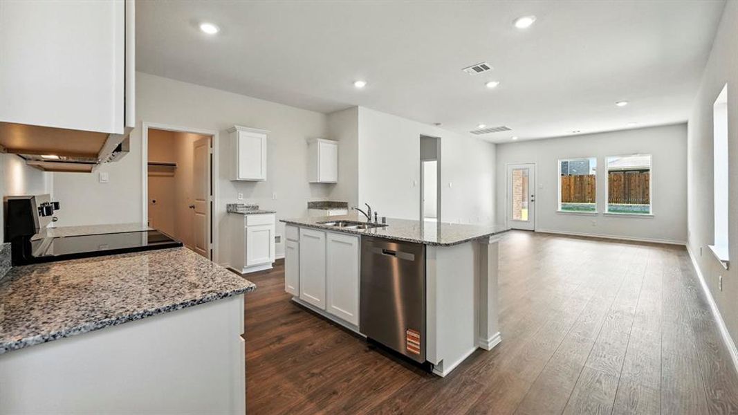 Open-concept kitchen and living area featuring white cabinetry, granite countertops, stainless steel appliances, and wood-finish flooring