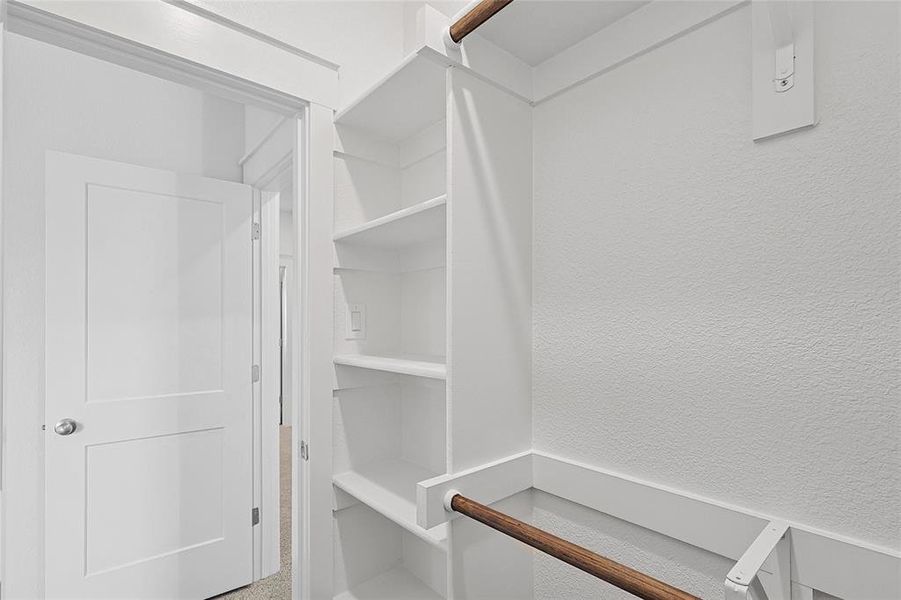 This closet features built-in white shelving, a wall-mounted light switch, and a closet rod
