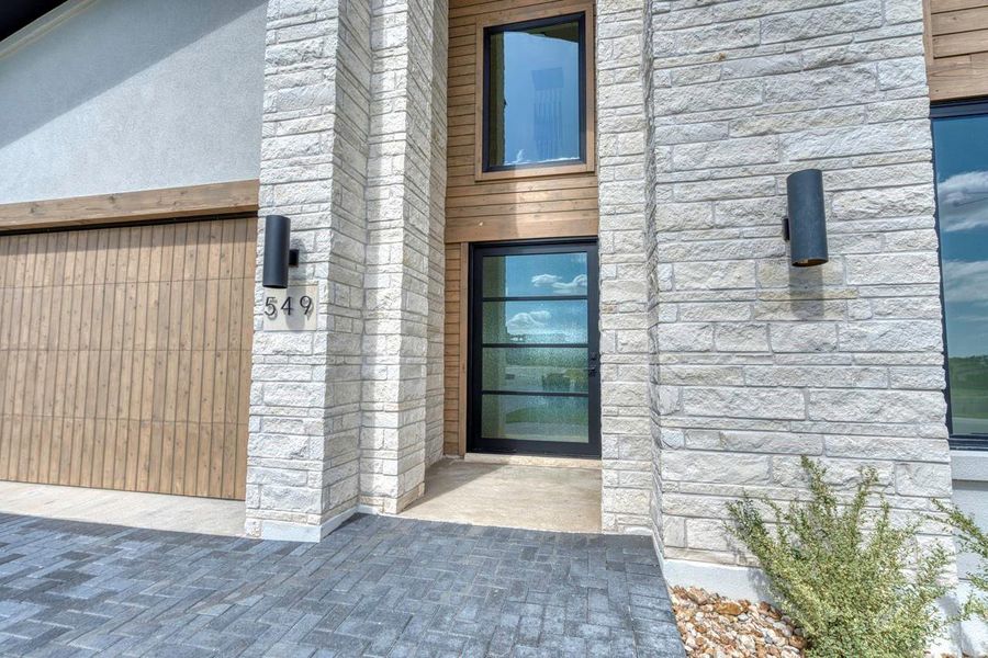 Natural stone columns frame a modern glass entry door and paved driveway.