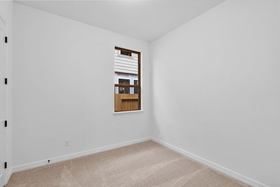 A comfortable third bedroom with plush carpet, a sun-filled window, and ample closet space.