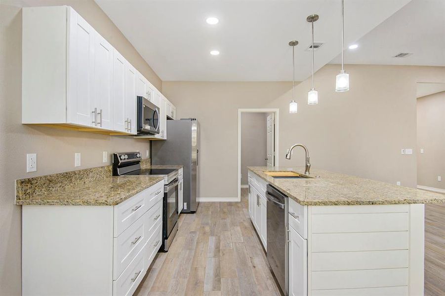 Kitchen featuring stainless steel appliances, light wood-style flooring, white cabinetry, a center island with sink, and light stone counters