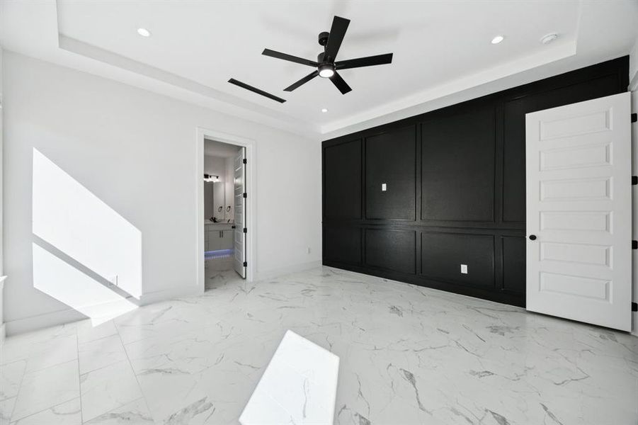 Unfurnished bedroom with light marble finish flooring, ceiling fan, ensuite bathroom, recessed lighting, and a raised ceiling
