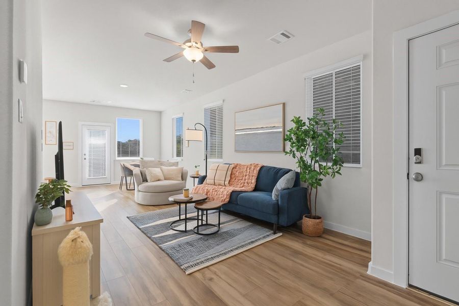 Bright and inviting living space with modern decor, featuring a cozy blue sofa, stylish round chair, and a sleek floor lamp. The room has large windows, a ceiling fan, and wood flooring, creating a warm and airy atmosphere.