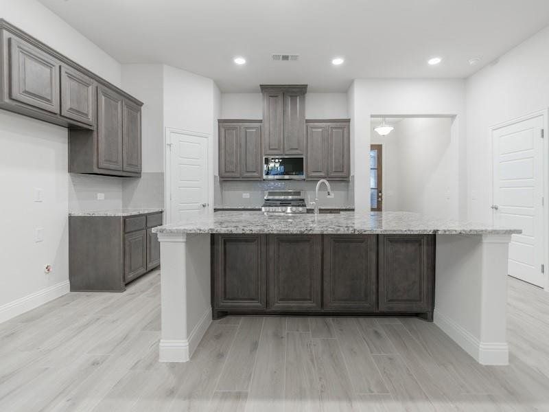 Kitchen with light stone counters, stainless steel appliances, and a center island with sink