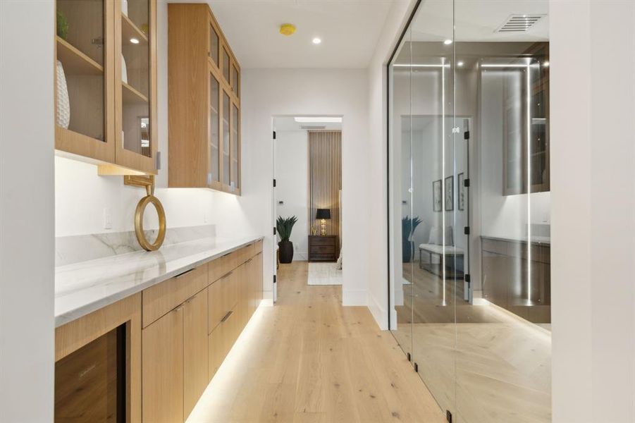 Large coffee bar just outside owners suite with beverage refrigerator, under cabinet lighting, stone countertops, and white oak flooring. Large coffee bar just outside owners suite with beverage refrigerator, under cabinet lighting, stone countertops, and white oak flooring.