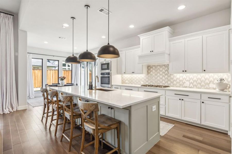 Kitchen with white cabinets, an island with sink, sink, decorative light fixtures, and light wood-type flooring