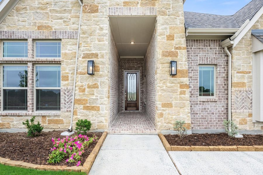 Home entrance with stone and brick exterior, covered entryway, wood front door with glass panels, and wall sconce lighting