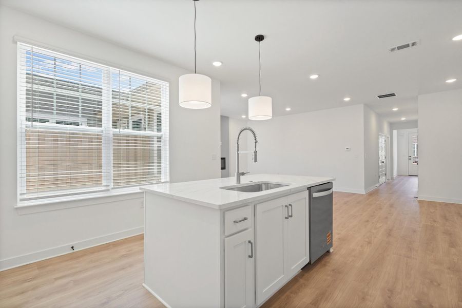 Kitchen island featuring a stainless steel sink with gooseneck faucet, white shaker cabinetry, and a dishwasher