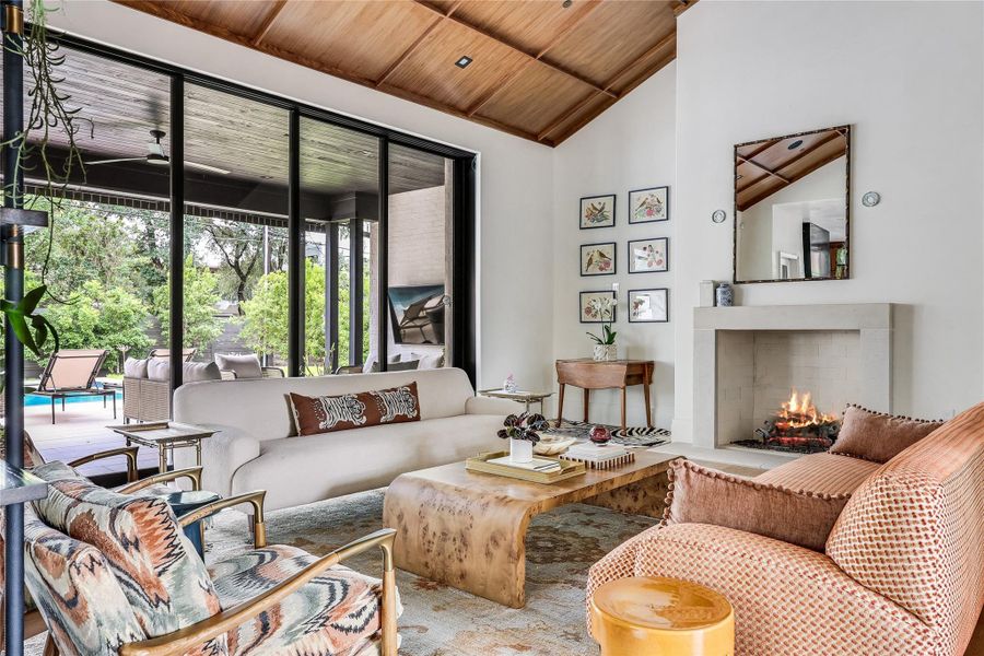Natural light floods this living space, featuring a cozy fireplace and expansive views of the outdoor pool area.