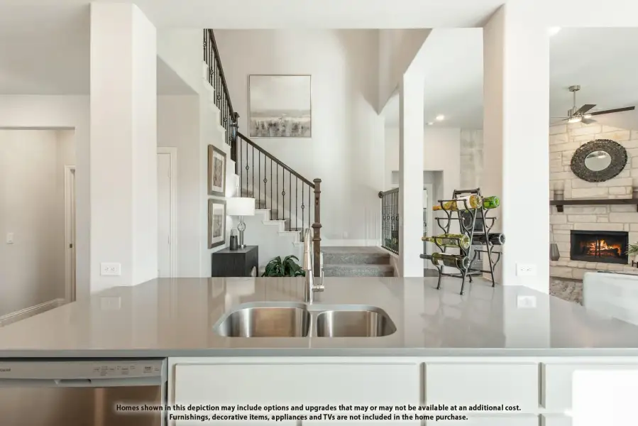 Kitchen island with double sink overlooking open living area with staircase and stone fireplace