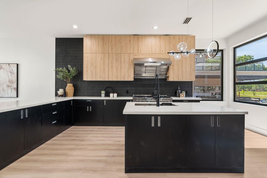 The island's undermount sink and matte black gooseneck faucet anchor this view, with globe-style pendant lights marking the center of the kitchen above. This centered island offers additional storage space in this already expansive kitchen.