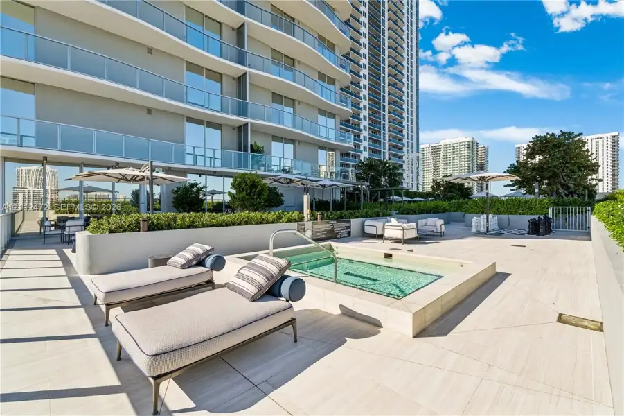 Outdoor terrace featuring an elevated spa, large-format stone-finish tile flooring, and integrated shrubbery planters