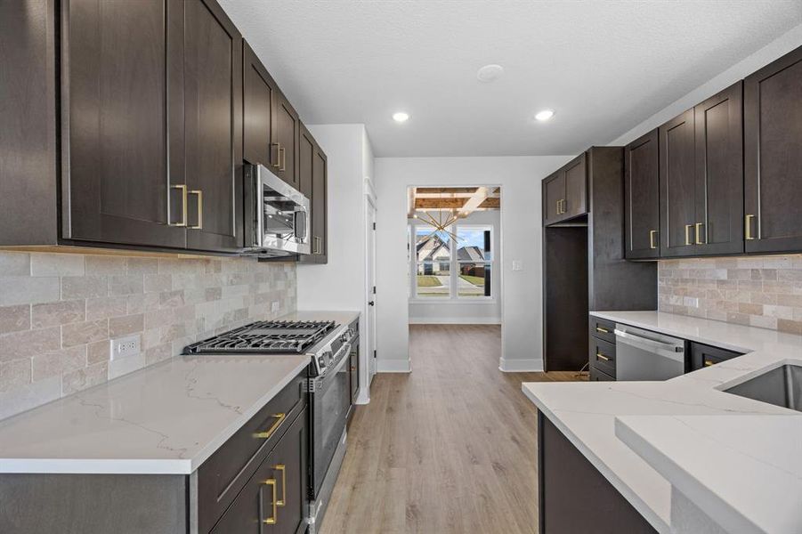 Kitchen featuring decorative backsplash, stainless steel appliances, dark brown cabinetry, light stone counters, and recessed lighting